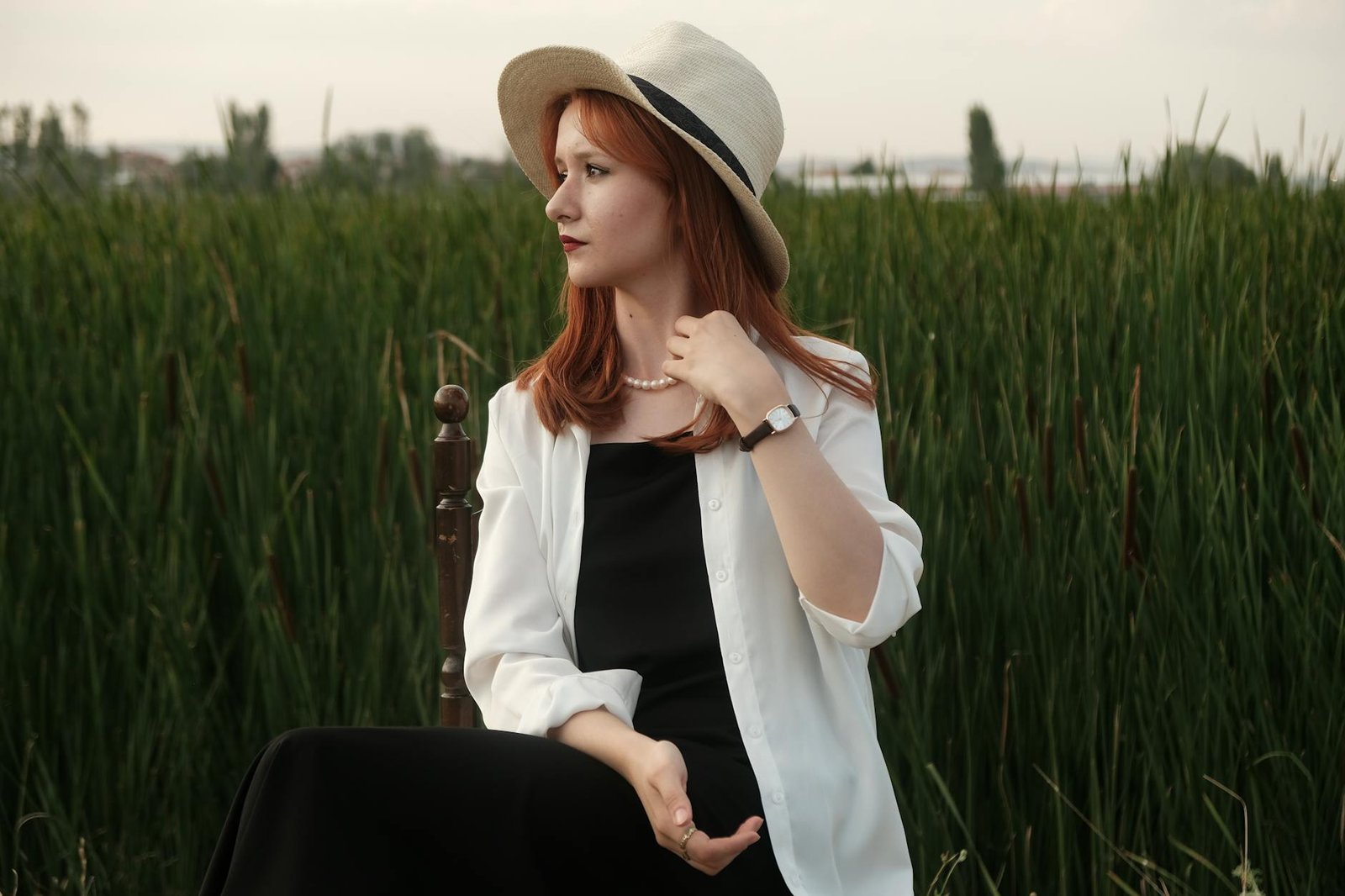 A fashionable woman wearing a sunhat and white shirt poses elegantly in a lush summer field.