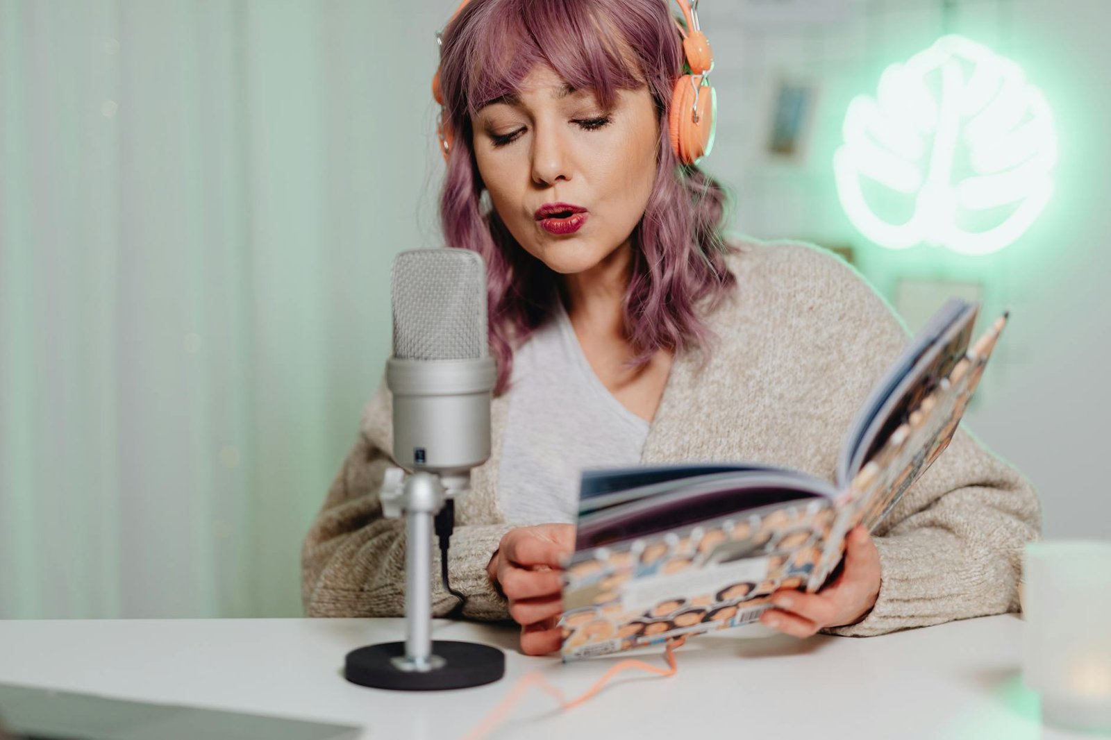 A woman podcasting while reading a book, wearing orange headphones.