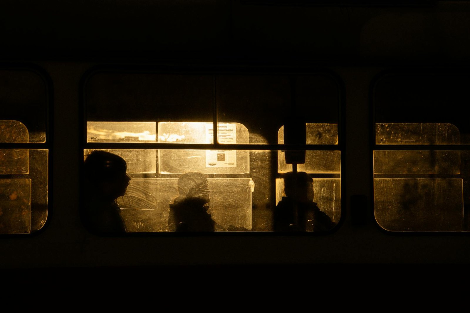 Passengers' silhouettes on a tram during sunset in Kyiv, casting a warm, moody glow through the windows.