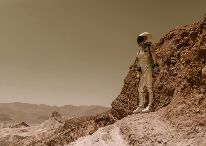 A lone astronaut in a spacesuit stands on a rugged, rocky terrain resembling an alien planet.