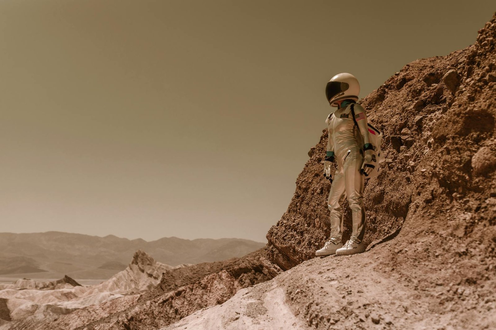 A lone astronaut in a spacesuit stands on a rugged, rocky terrain resembling an alien planet.