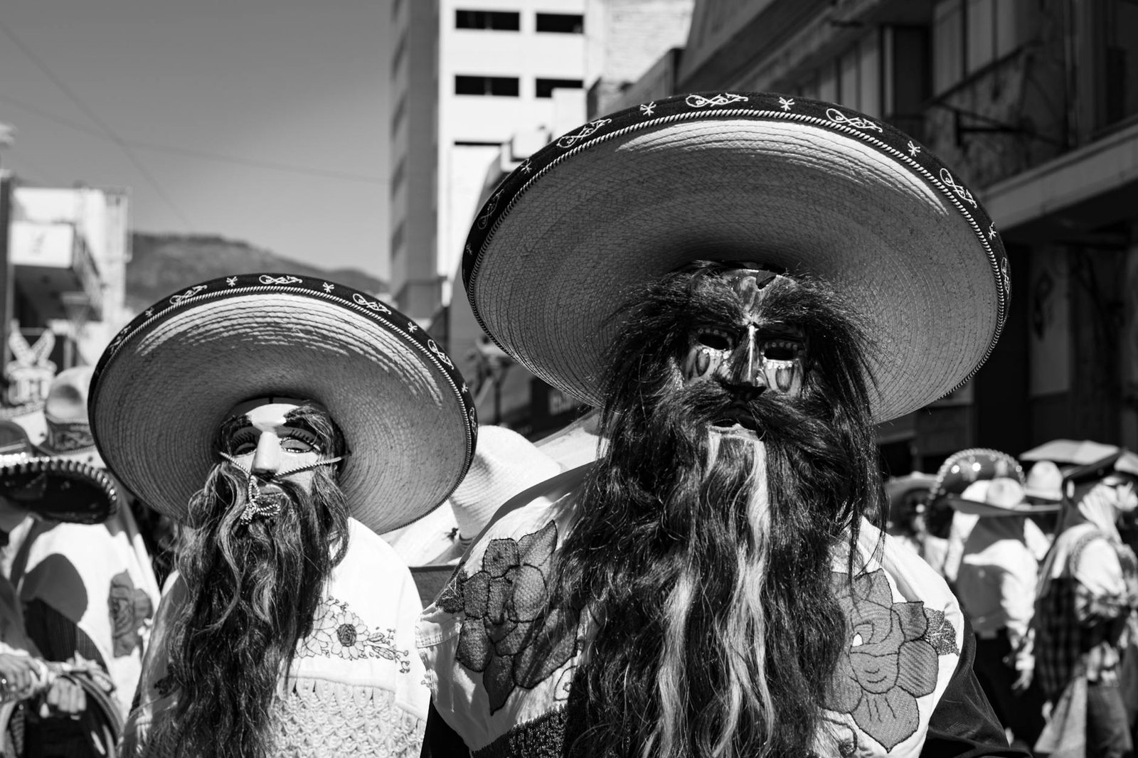 Black and white photo of a traditional Mexican parade in Pachuca de Soto, featuring masked participants with sombreros.