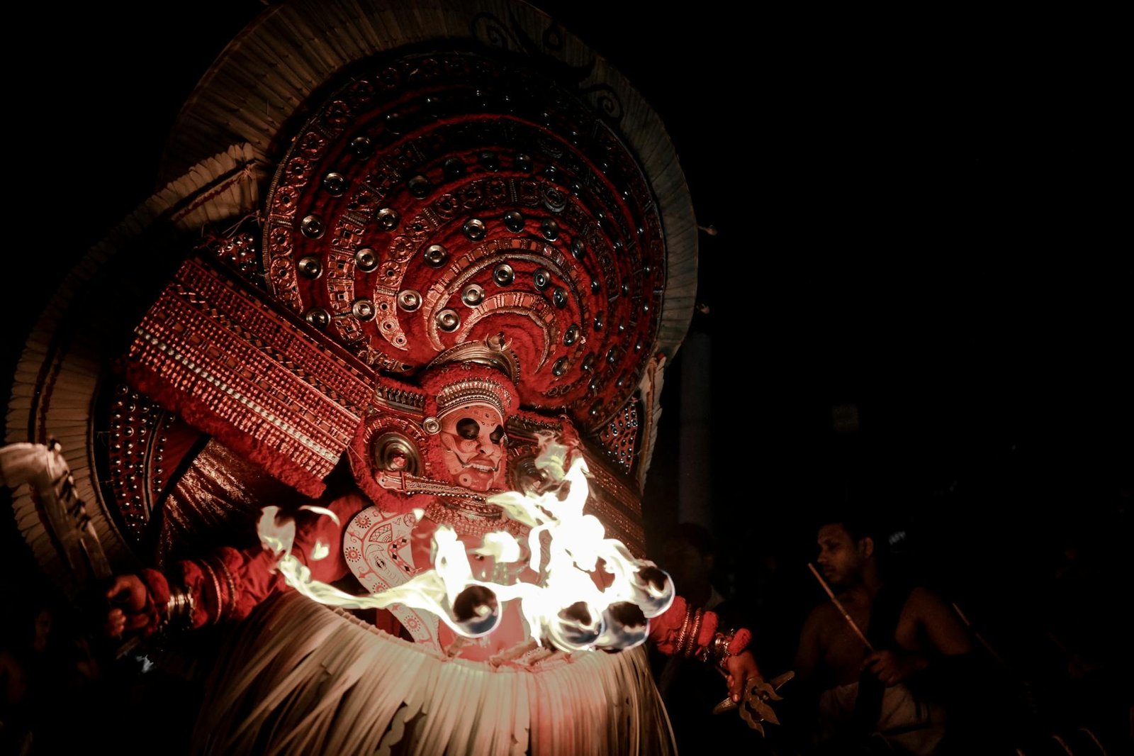 A captivating Theyyam performance featuring vibrant costumes and fire rituals under the night sky.