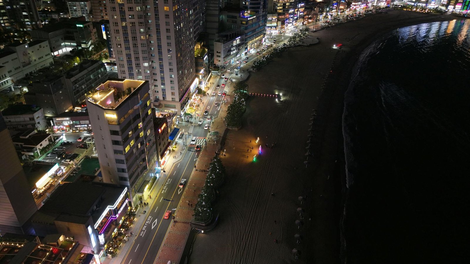 Stunning aerial night view of Haeundae Beach, Busan, showcasing vibrant city lights along the coastline.