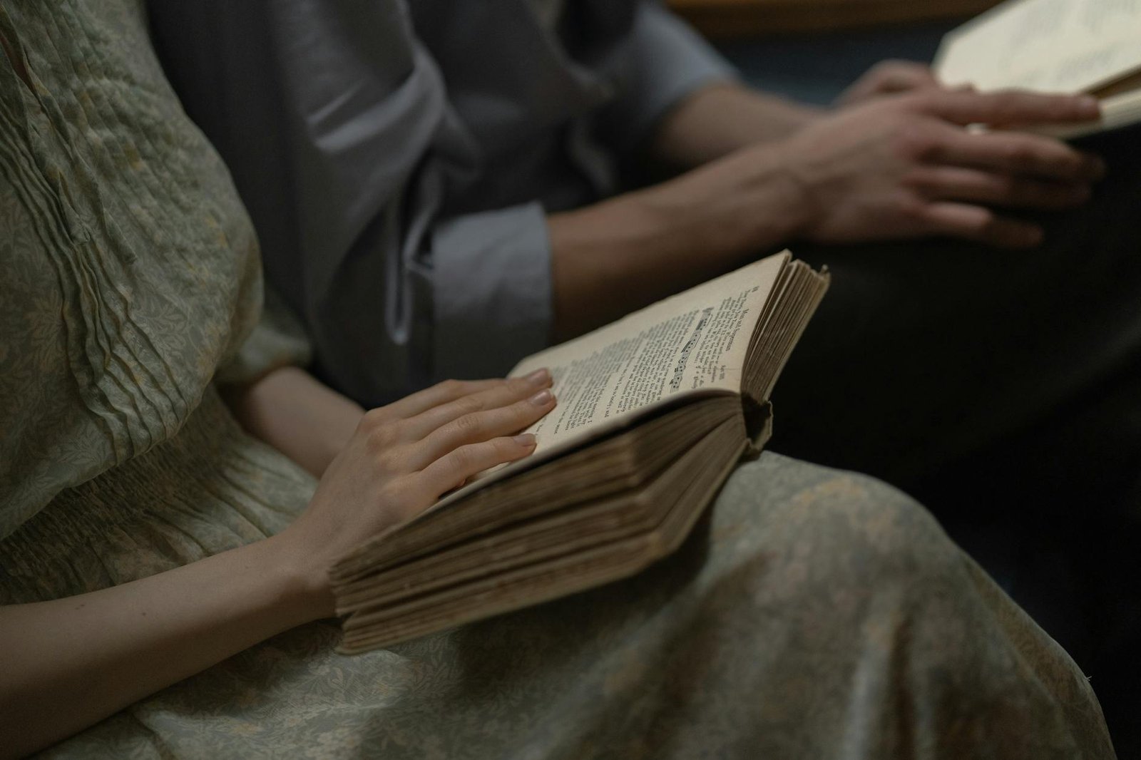 Close-up of two people reading an antique book, focusing on the hands and text.