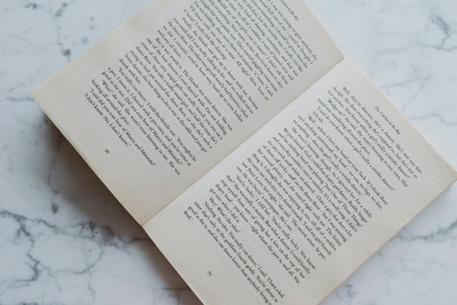 Top view of opened fiction book in soft binding lying on marble table