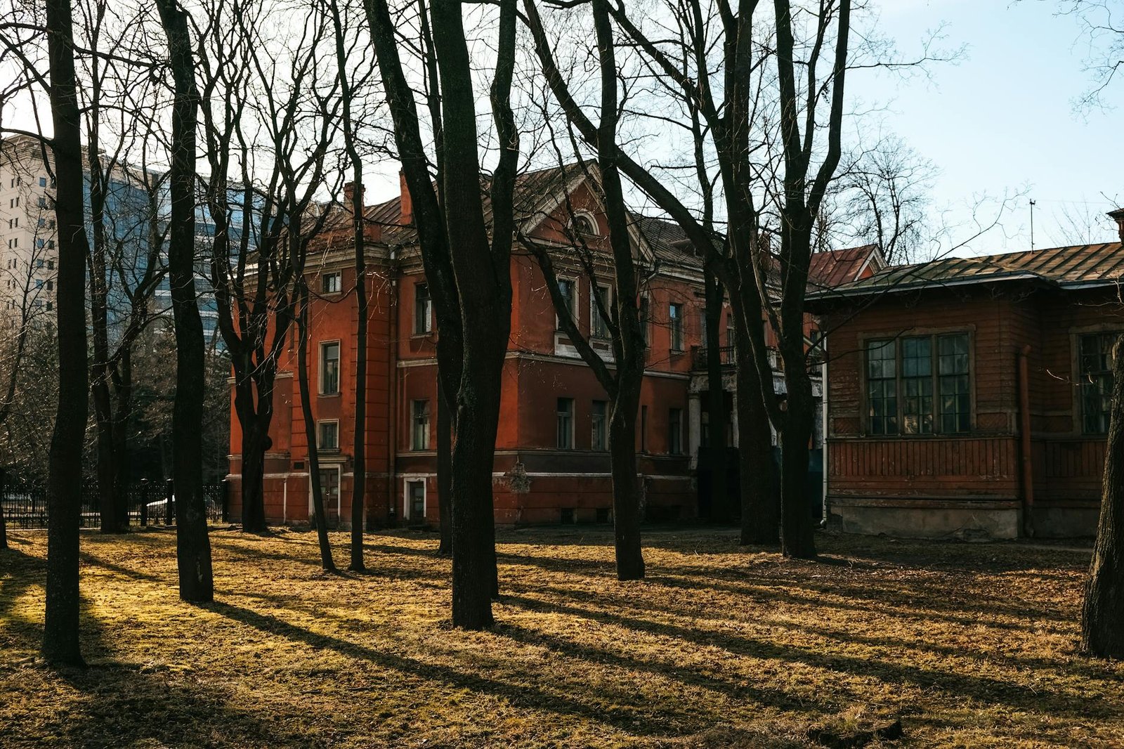 Historic red building surrounded by leafless trees in winter sunlight.