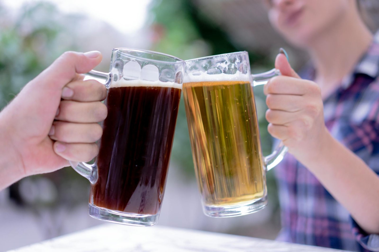Close-up of hands holding mugs of dark and light beers in a cheerful toast.