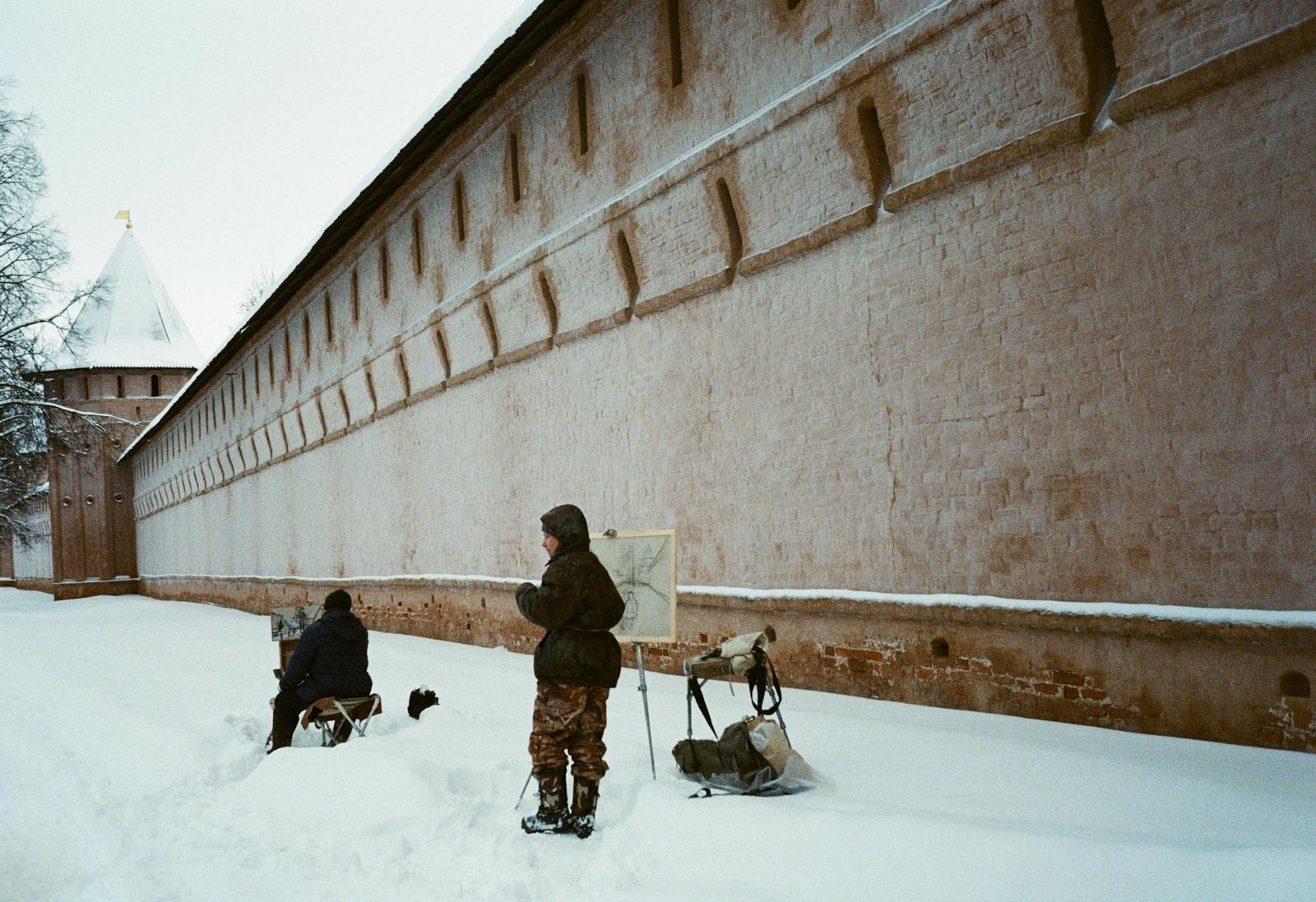 Artists painting by a snowy historic wall in Suzdal, capturing winter scenes.