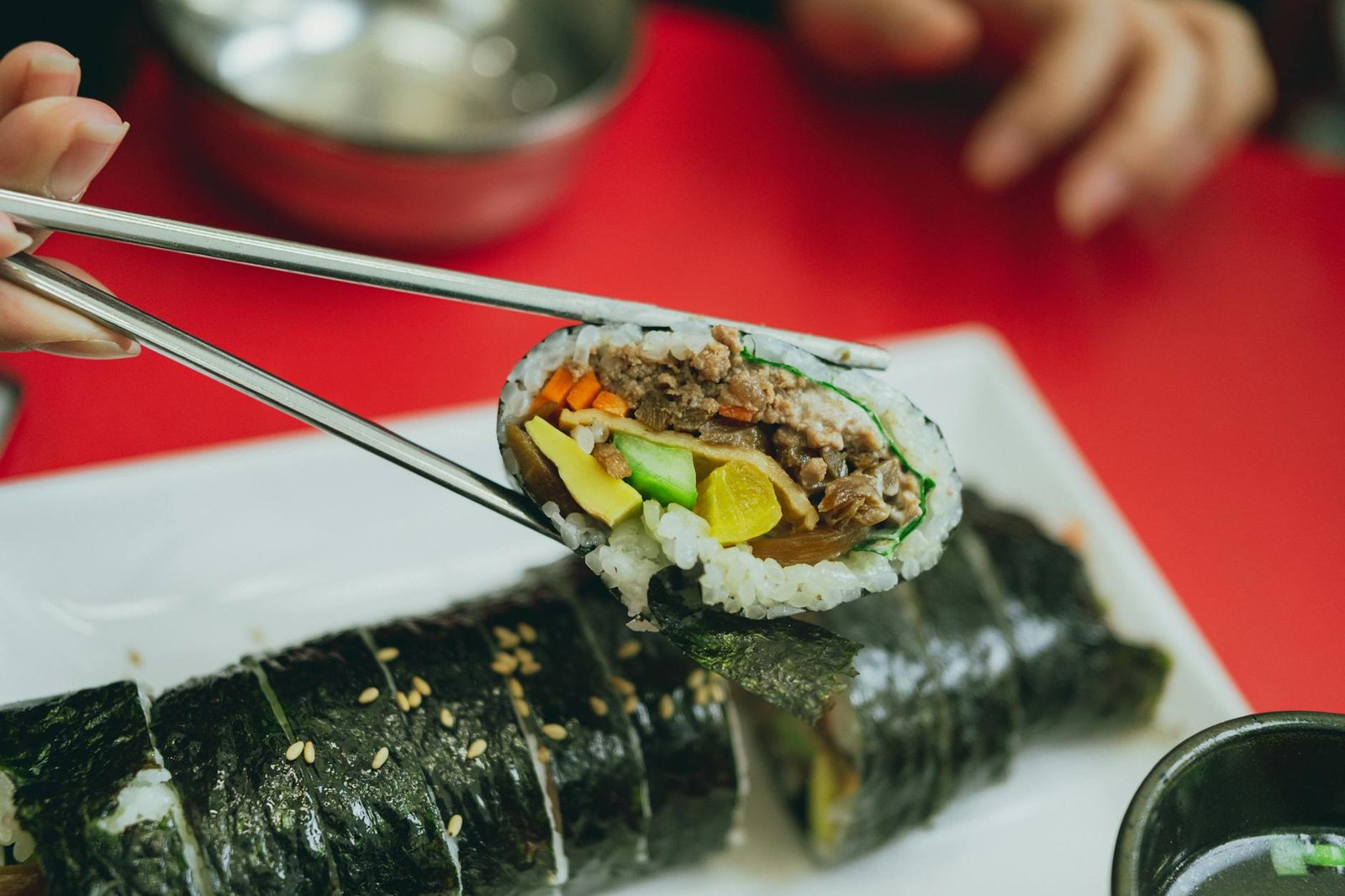 A close-up of a tasty Korean gimbap roll held by chopsticks, showcasing fresh ingredients.