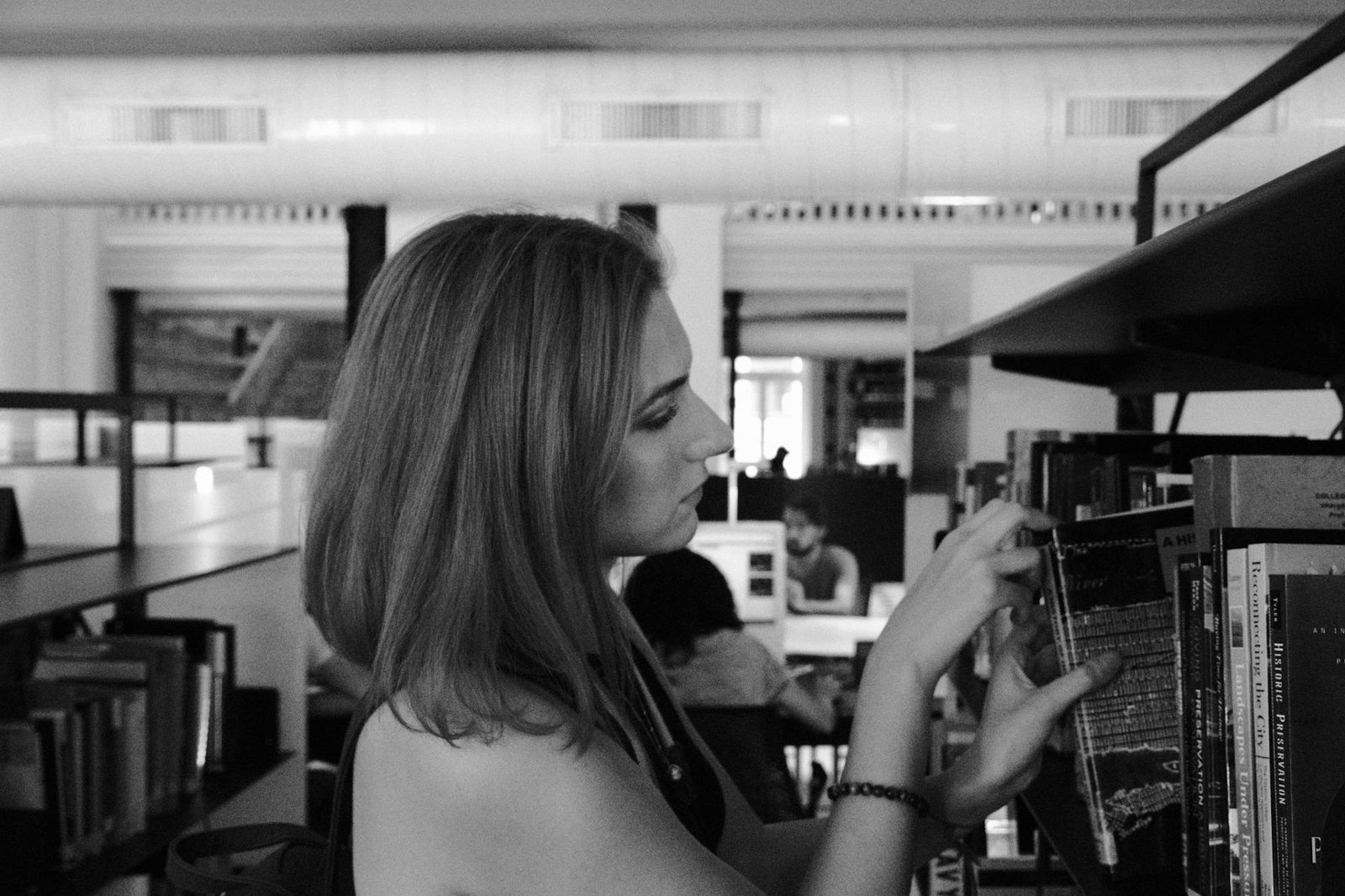 Young woman selecting a book from a shelf in a spacious Istanbul library, emphasizing knowledge and education.